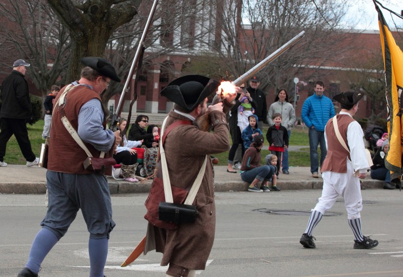 Families stationed in front of Arlington High School for the Patriots' Day Parade watch as gunpowder ignites in the musket of one of the Menotomy Minutemen. April 14, 2013.