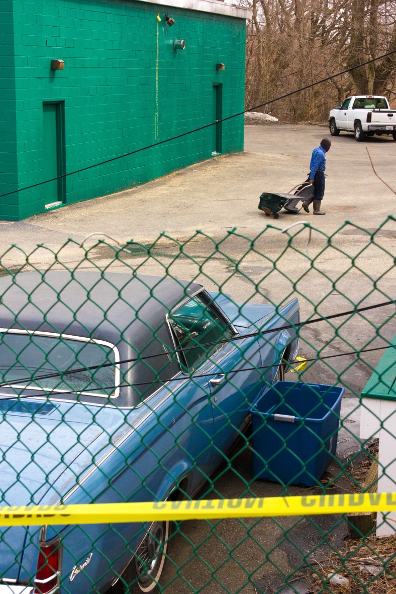 A man lugs car parts across the back lot of Dudley Street Auto Body. March 28, 2014.