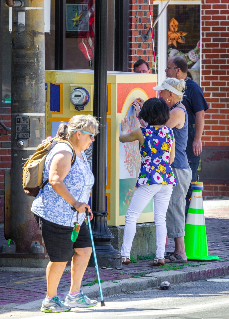 An artist works on her painting, making a colorful attraction of a once drab utility box in Arlington Center. June 27, 2014.
