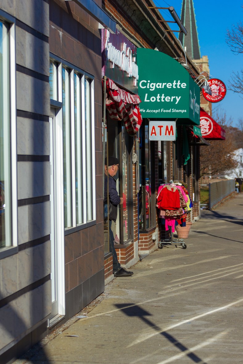 A man stands in the front entrance of a Medford street shop while smoking a cigarette. November 29, 2014.