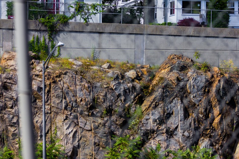 Just below frame, cars whiz through what was once solid rock, but is now a canyon-like section of Route 2. Above it all, Arlington homes along an exit ramp. August 05, 2015.